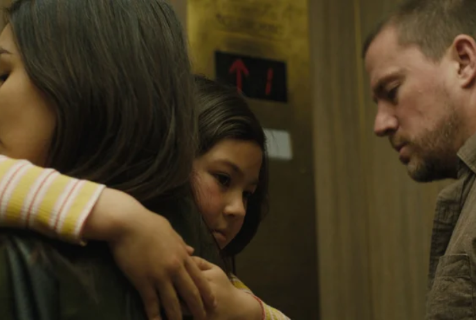 A young person hugs an older person while another person looks on outside of an elevator.