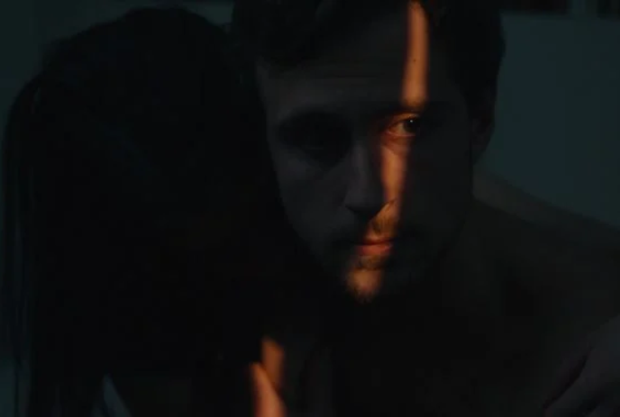 A person in the shadows is illuminated by a small crack of light.