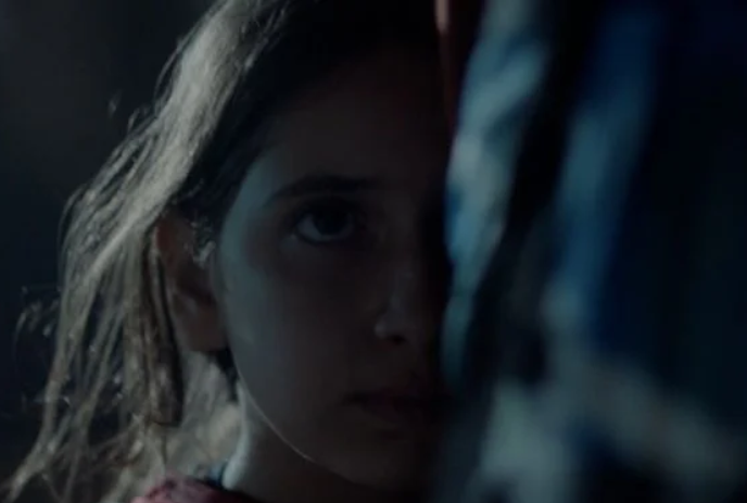 A young person looks pensive while standing in front of someone else.