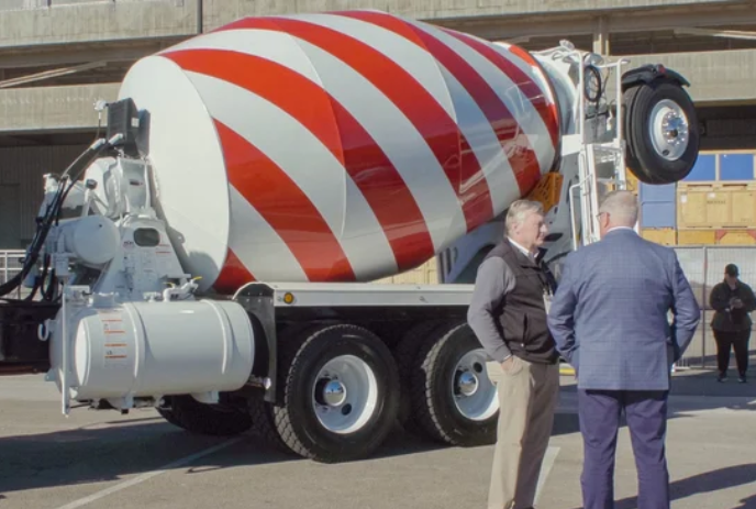 Two people stand in front of a red and white cement mixer truck in a deep discussion.