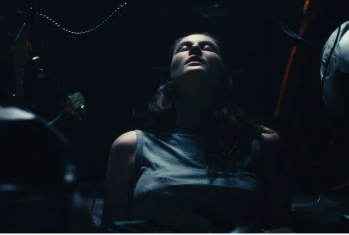A person in a dark area sits with their eyes closed.