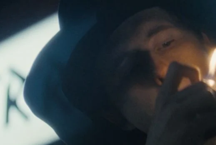 A person wearing a wide-brimmed hat lights a cigarette.