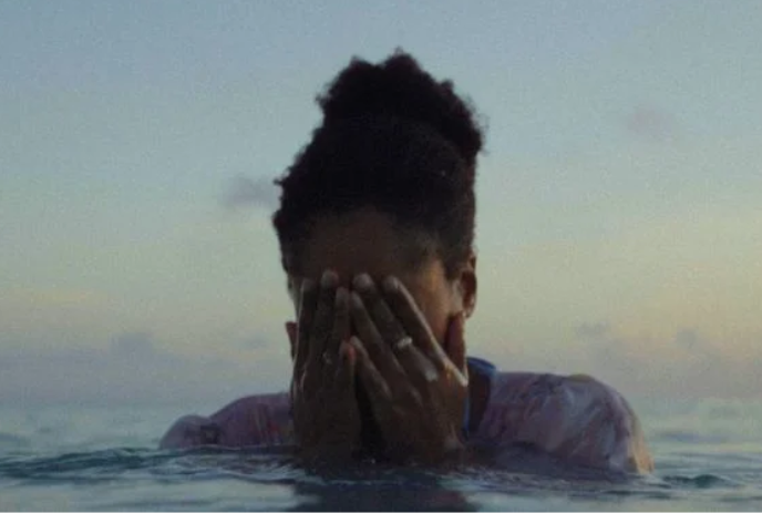 A woman stands in the water with her hands covering her face.
