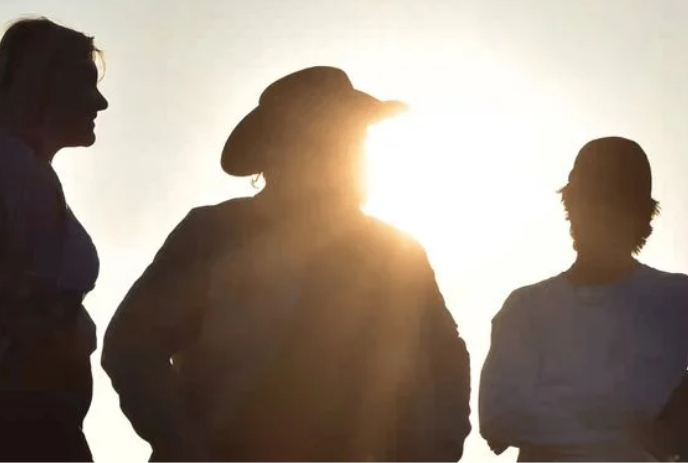 Three people stand with the sun behind them so their faces are shadowed.