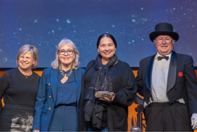 Four smiling people stand together as winners in front of a big screen.