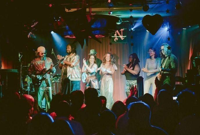 Band performing on colorful stage with retro outfits as crowd watches lively concert scene.