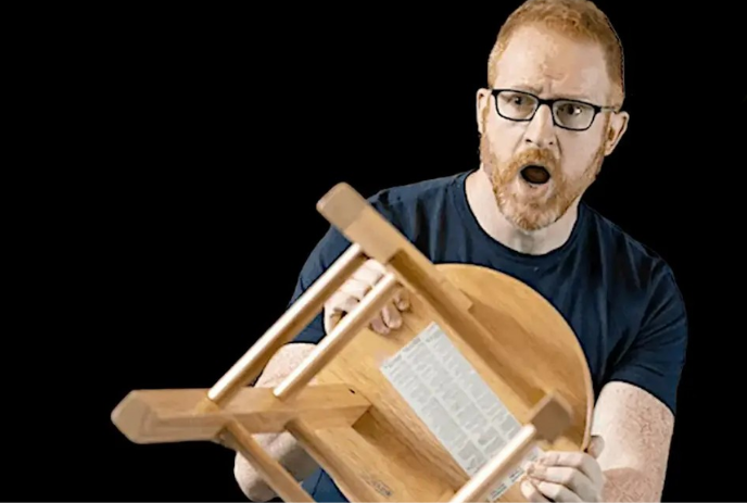 A person holds a stool in front of themselves and has a scared look on their face.