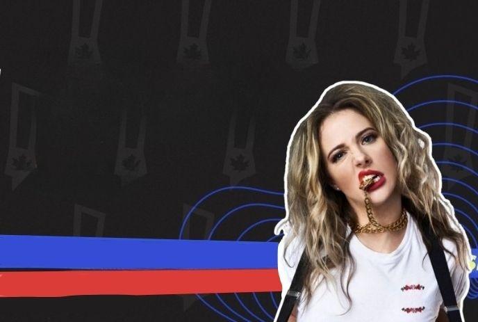 Brittany Schmitt with long wavy hair holding gold chain, wearing white shirt and suspenders against dark graphic backdrop.