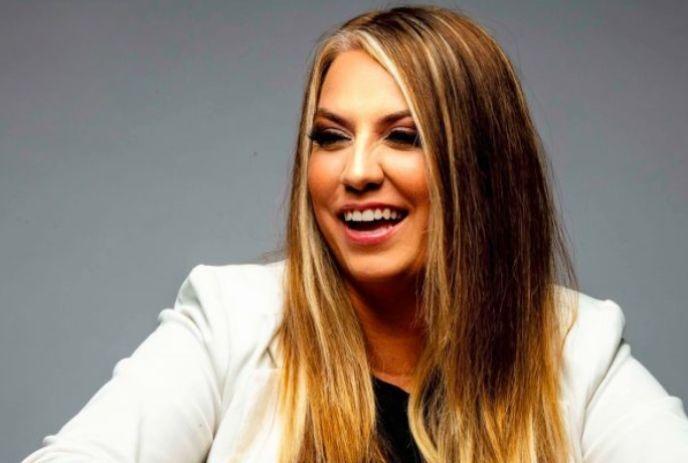 Artist Laura Gagnon with long hair in a white blazer against a gray background.