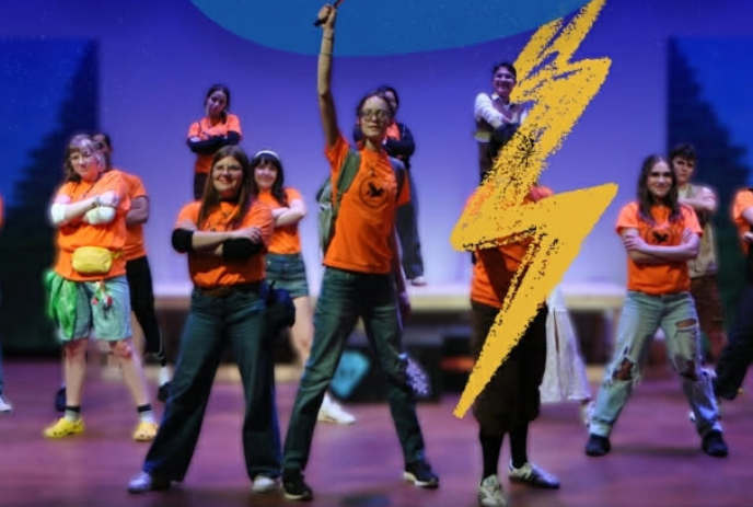 A group of people stand onstage with one person raising their arm and a yellow lightning strike going across the image.