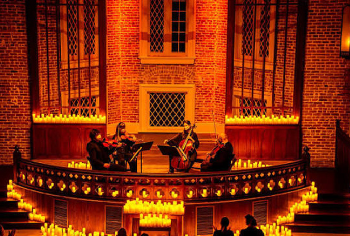 Four people sit onstage with their instruments while surrounded by candlelight giving off an orange glow.