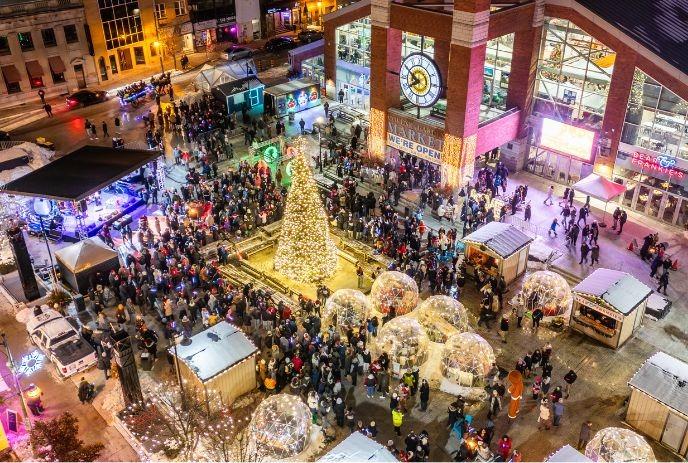 Crowds gather around a glowing holiday tree, festive domes, and market stalls at Covent Garden Market.