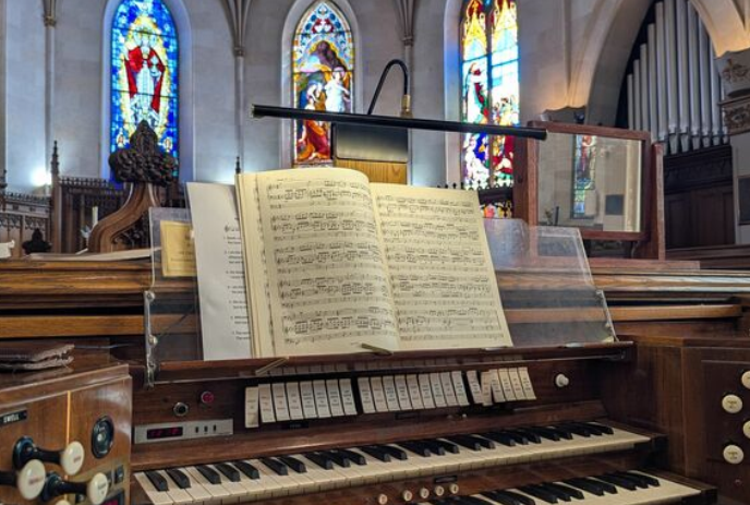 An organ sits in front of stained-glass windows inside.