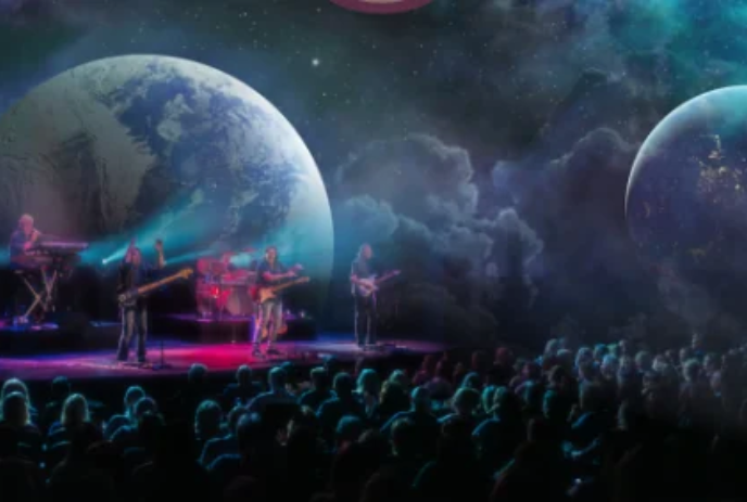 Band members on stage in front of a large audience, with images of the world behind them.