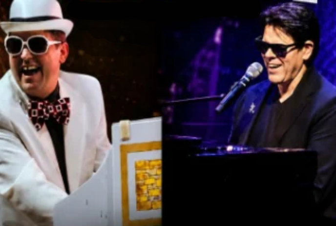 A person wearing a white suit with white glasses and a white hat sits at a piano in front of a person wearing black with black glasses.