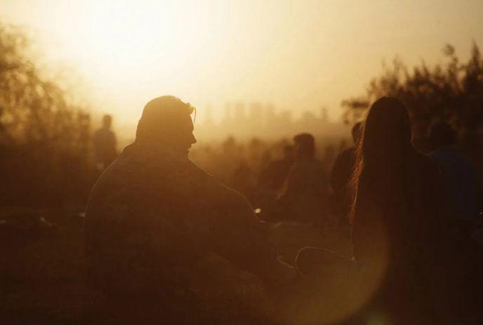 A warm sunset silhouette of people seated outdoors with a hazy city skyline glowing behind them.