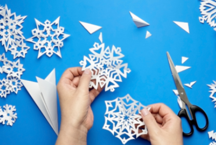Child's hands holding different snowflake cutouts against a turquoise blue background..