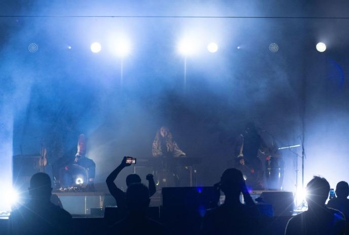 A band performs on stage amidst vibrant lights and smoke, while the audience enjoys and records the moment.