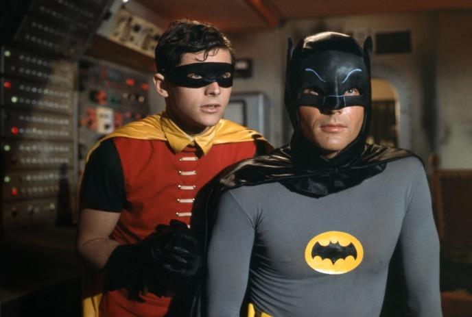 Masked duo of Batman and Robin standing in control room with colorful panels behind them.