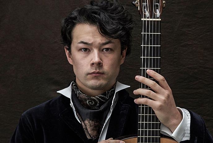 Stoic person sits with their guitar in front of them.