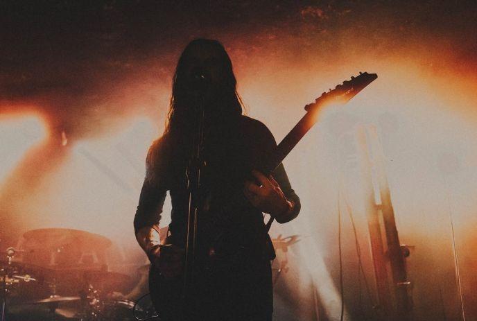 Silhouetted guitarist performing on stage under bright lights, smoke effects.