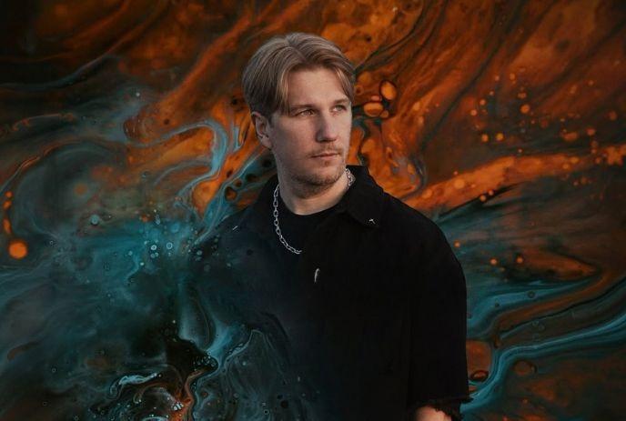 Person in black attire against a swirling abstract backdrop of blue and orange tones.