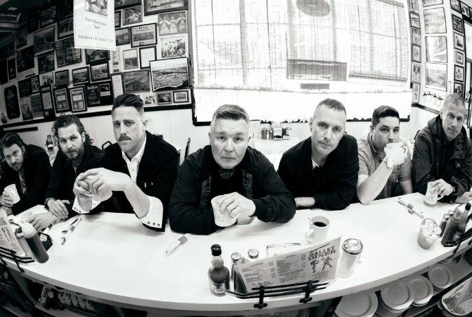 Seven band members seated at a diner counter in a black-and-white wide-angle photo.