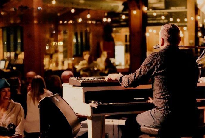 Pianist performs on a warmly lit stage before a seated audience in a cozy venue with ambient lights.