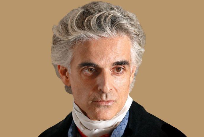 Portrait of a man with silver hair, formal attire, and a neutral beige background.