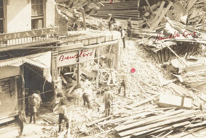 Sepia image of broken buildings with people walking around outside of them.