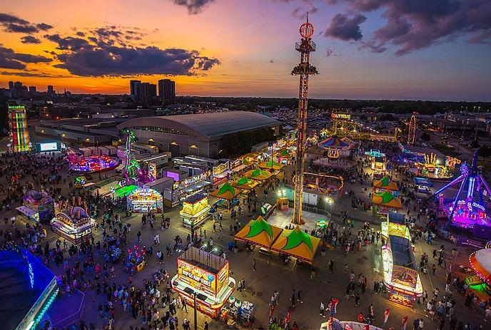 Aerial view of a previous Western Fair, vibrant with colourful lights, rides, and booths.