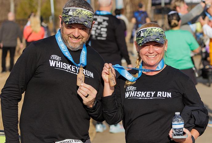 A man and a women showing off their medals from a previous Whiskey Run.