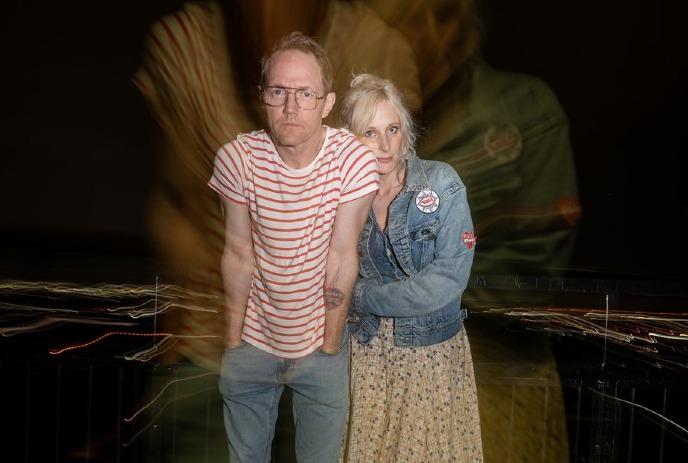 Whitehorse in a striped shirt and Chloe Doucet in a denim jacket stand closely, looking forward.