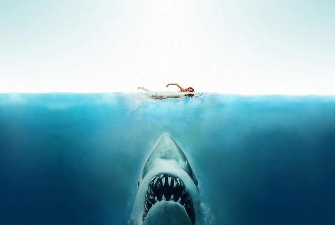 A woman swimming in the middle of a deep blue ocean, beneath her, a giant shark with an open mouth, ready to attack.