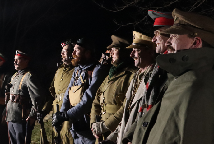 Men in uniforms stand in line outdoors at night, smiling against dark background.