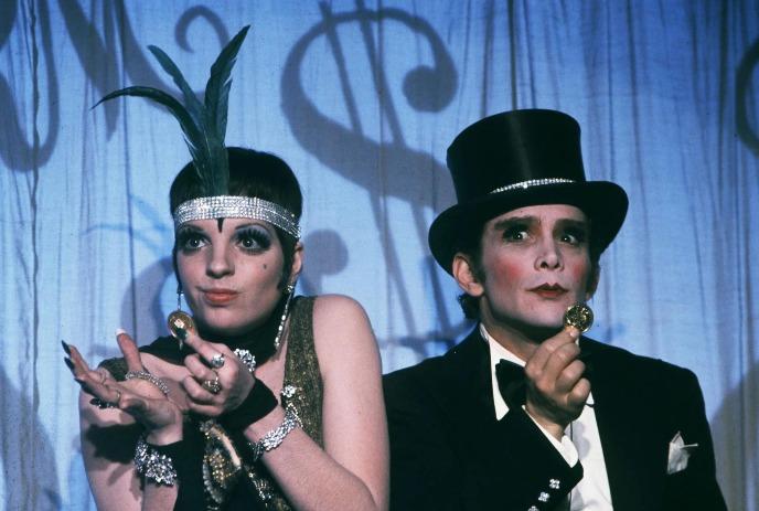 Two people in vintage attire, one with a feathered headband, the other in a top hat, against a musical backdrop.