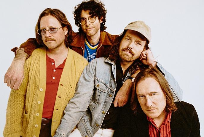 Four artists in colourful outfits, under a white background posing for a picture.