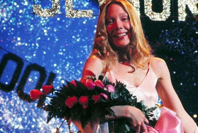 Smiling young person in pink dress holds bouquet of roses on glittery stage, celebrating at a festive formal event.