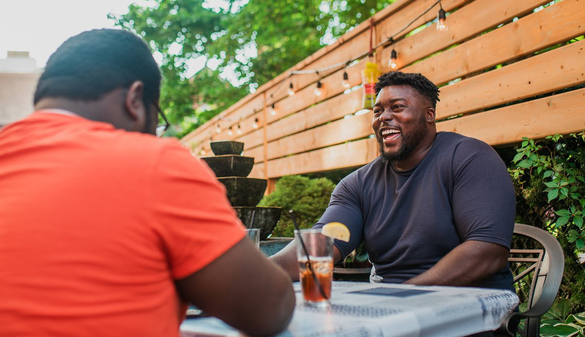 two people sitting at a patio table having a conversation enjoying a drink
