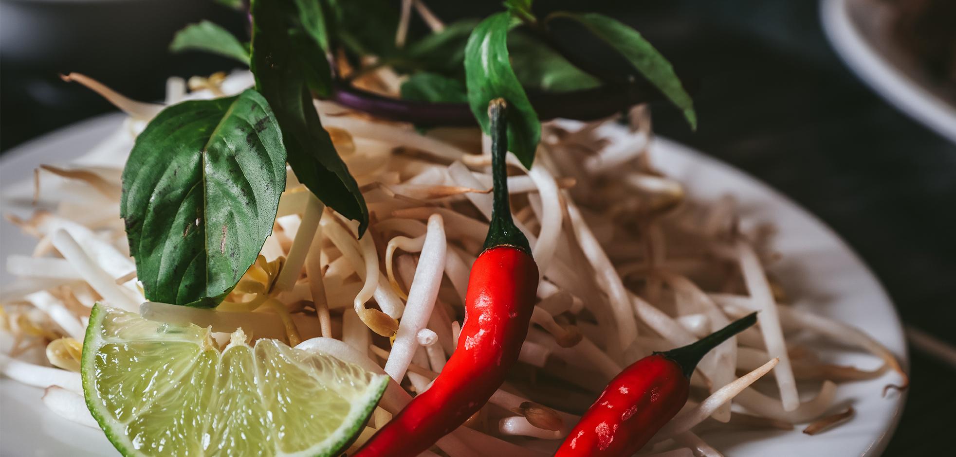 a plate of bean sprouts with chili peppers and wedge of lime