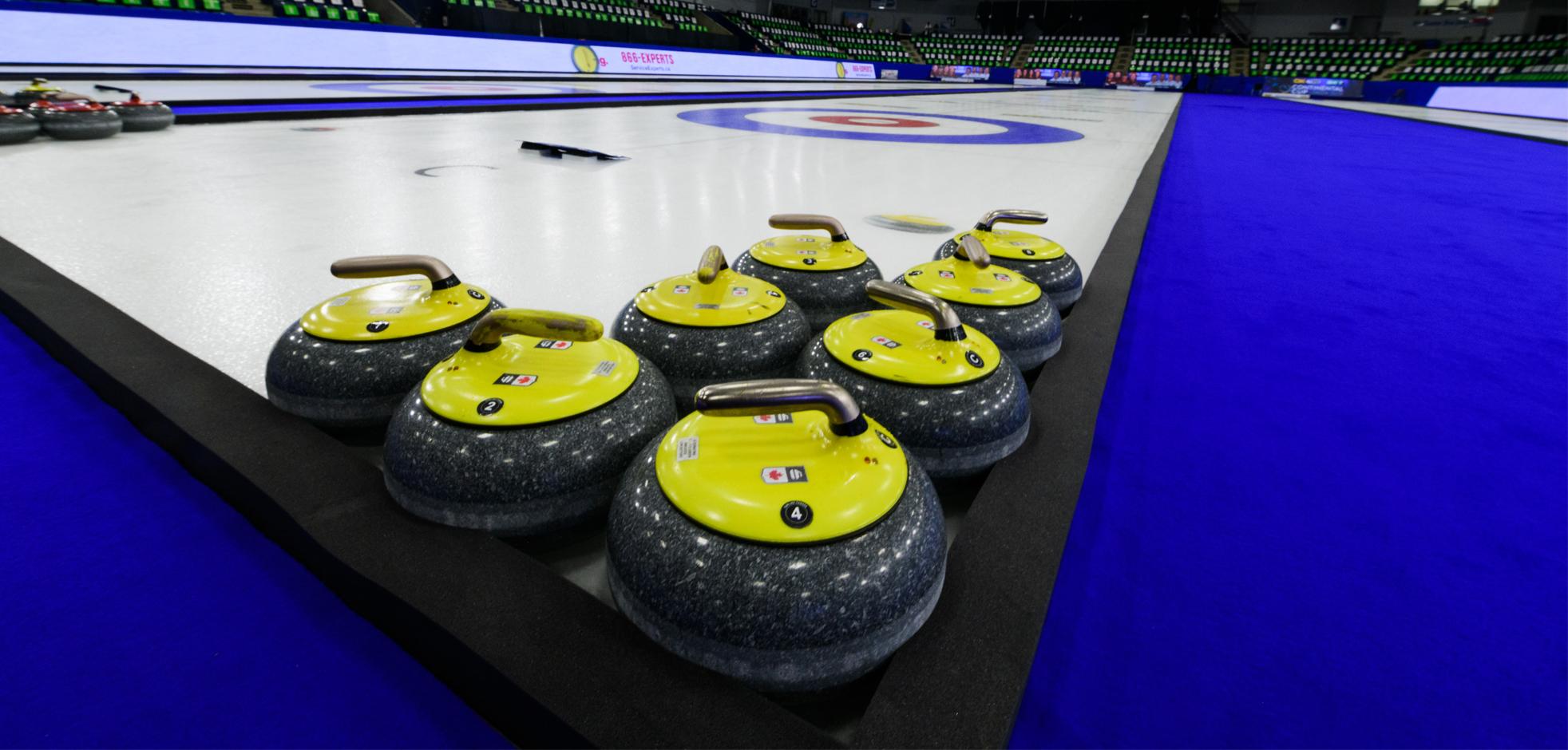 A group of curling stones tucked into a corner of an ice rink.