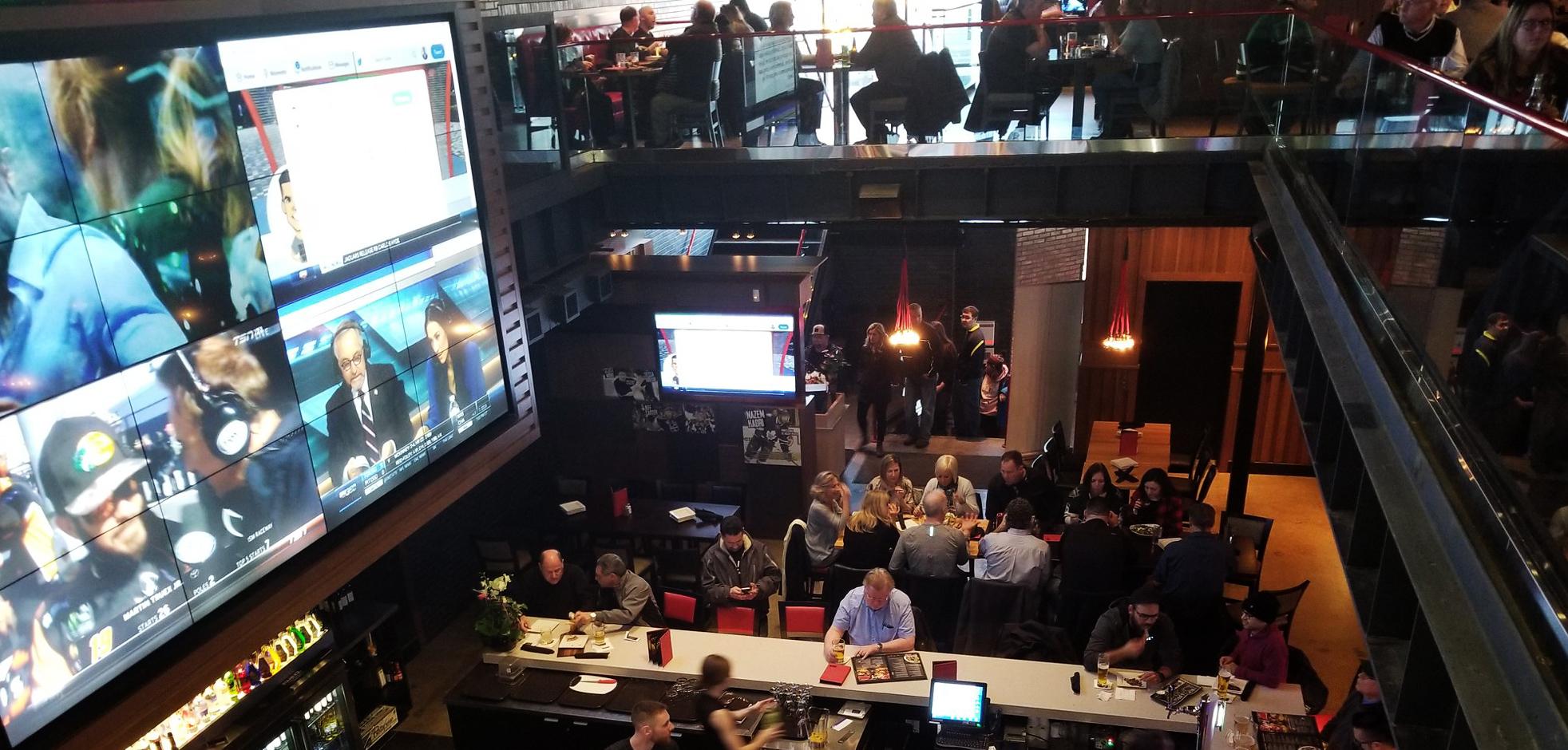 Overhead interior view of a sports bar in London, Ontario with large tv screens and various people sitting at tables and a large bar.