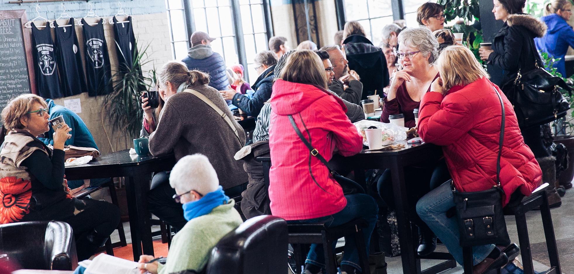 Groups of people seated and enjoying coffee and food at the The Market at Western Fair District.