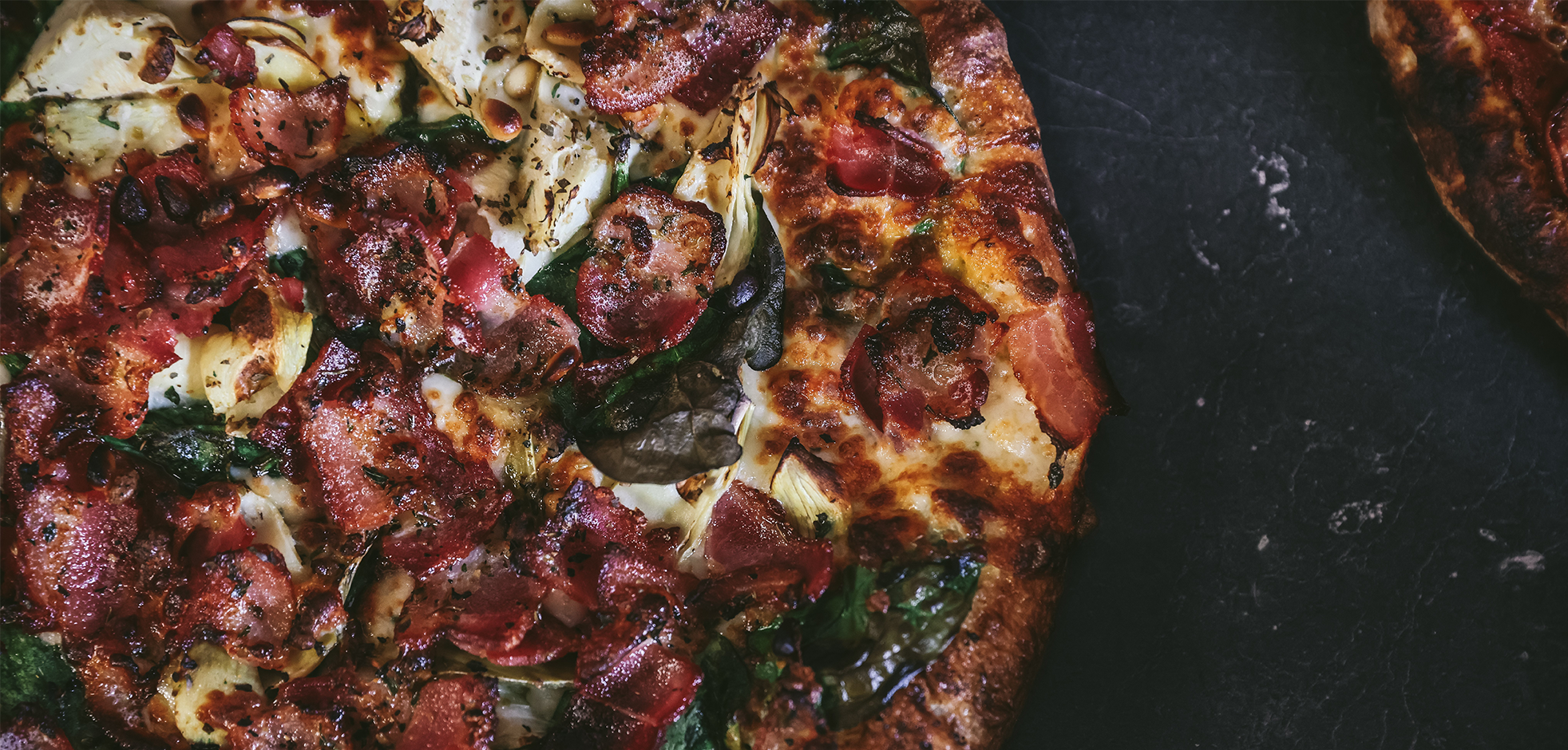 aerial view of a pizza on a black marble table loaded with pepperoni, sausage and basil