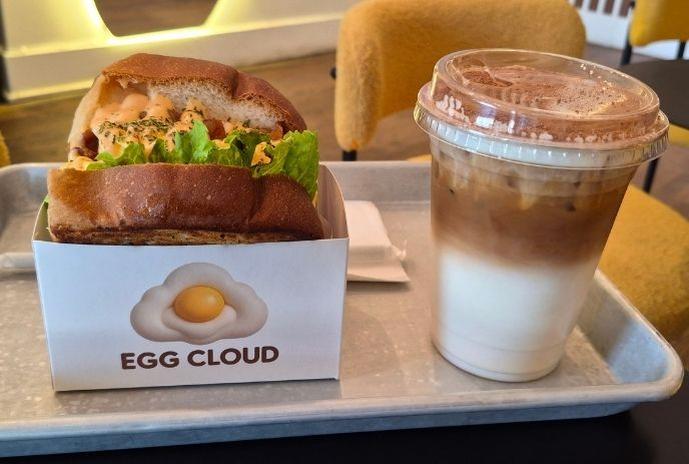 Egg Cloud sandwich topped with sliced avocado in a takeout box.