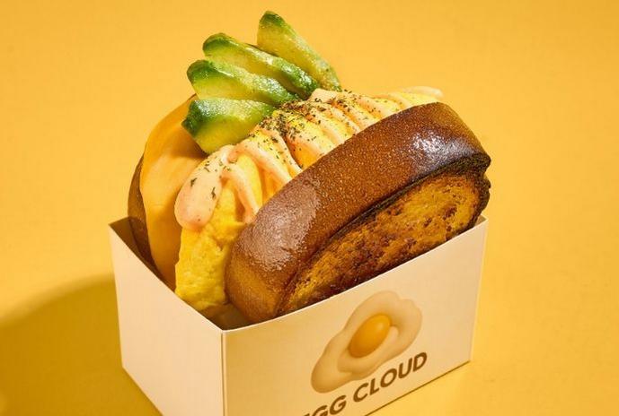 Egg Cloud sandwich topped with sliced avocado in a takeout box.