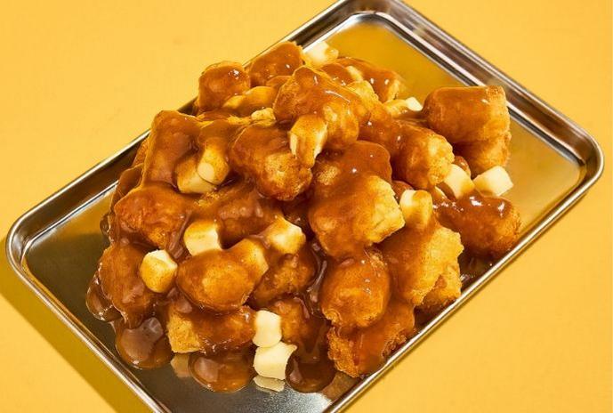 Crispy fried Egg Cloud potato bites topped with sauce, served in a metal tray on a yellow background.