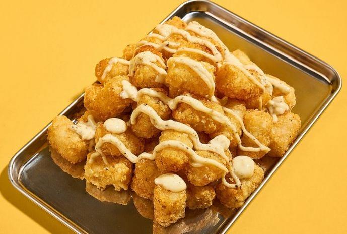 Golden waffle fries drizzled with sauce and topped with cheese curds in a metal tray.