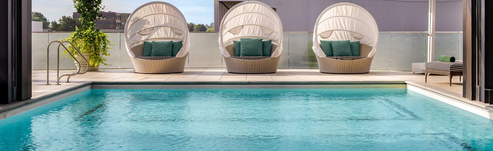 Outdoor pool with shaded wicker loungers, green cushions.