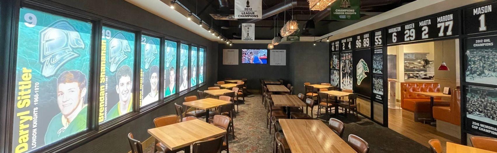 sports themed room with tables chairs and london knights banners and player displays on walls around the space light.